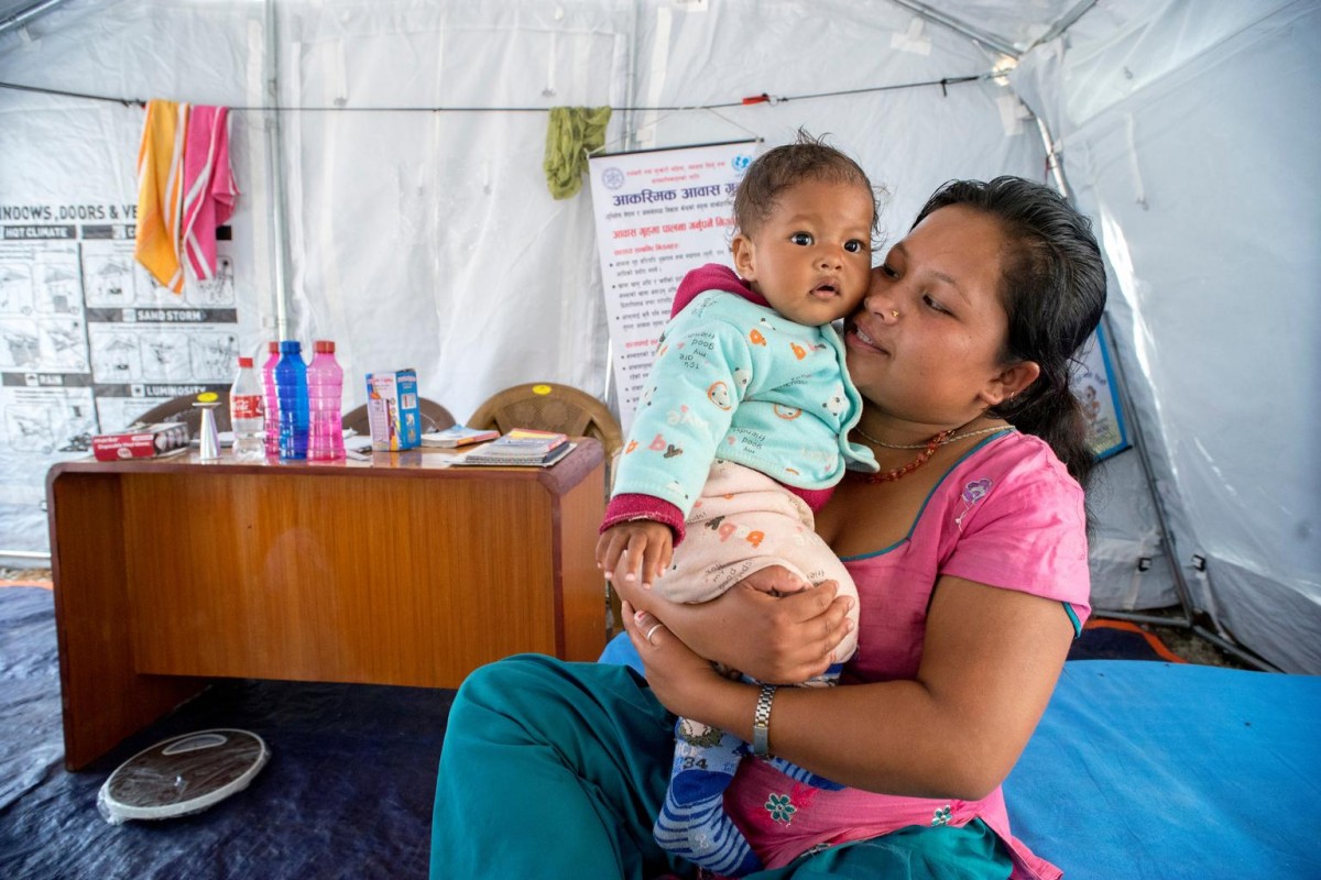 On 25 May, Preeti Thami, 19, sitting on a bed, holds her 8-month-old baby, Rashmi, in a UNICEF-supported shelter home set up on the grounds at the District Health Office in the town of Charikot in Dolakha District, epicentre of the 12 May earthquake. Preeti and Rashmi, who are from the village of Ahlampur (also in the district), lived in the open for a month after their home was destroyed during the massive 7.8-magnitude earthquake in April. The young woman managed to flee the dwelling with her baby just before it collapsed. UNICEF and partners are also providing hygiene and nutrition supplies across quake-affected areas of the country.

In late May 2015 in Nepal, humanitarian partners continue to scale up relief operations following the 7.8-magnitude quake that struck on 25 April and the 7.3-magnitude quake that hit on 12 May. As of 27 May, more than 8,670 people have been killed and 21,933 people have been injured in the disaster. In the 14 districts hardest hit, 2.8 million people, including 1.1 million children, have been affected. Residences, schools and vital infrastructure, including hospitals, have also been severely damaged or destroyed in the disaster, leaving children and families homeless, vulnerable to disease outbreaks and in urgent need of food, shelter, safe water and sanitation, and health, protection and education support. With more than 760 thousand homes destroyed or severely damaged during the disaster, shelter remains a top priority. UNICEF, working with the Government and other partners, is supporting efforts across vital sectors, including shelter, water, sanitation and hygiene (WASH), nutrition, health, child protection and education. By 20 May, UNICEF had reached approximately 305,109 people with water interventions and provided 45,201 people with access to sanitation and handwashing facilities and 225,585 people with hygiene education and related materials. UNICEF and partners are also setting up shelter homes in affected areas, to provi