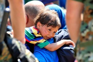 On 26 August, a distressed child rests over the shoulder of the man carrying him, in the town of Gevgelija, on the border with Greece. Uniformed officers from the special police forces of the former Yugoslav Republic of Macedonia stand nearby. In late August 2015 in the former Yugoslav Republic of Macedonia, more than 52,000 people have been registered at the border by police in the town of Gevgelija, after entering from Greece, since June 2015. Since July 2015, the rate of refugees and migrants transiting through the country has increased to approximately 2,000 to 3000 people per day. Women and children now account for nearly one third of arrivals. An estimated 12 per cent of the women are pregnant. Many are escaping conflict and insecurity in their home countries of Afghanistan, Iraq, Pakistan and the Syrian Arab Republic. There are children of all ages traveling with their families. Some are unaccompanied minors aged 1618 years who are traveling in groups with friends. They are arriving in the country from Greece, transiting to Serbia and further to Hungary, from where they generally aim to reach other countries in the European Union.