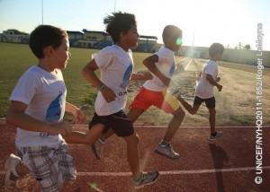 Boys run on a track at Guillermo Prospero Trinidad Stadium, in Oranjestad, the capital. They are participating in a programme offered by Athletik Bond, a local government-sponsored organization that coaches children in track and field sports. In September 2011, Aruba continues working to protect the welfare of its children since gaining autonomy from the Netherlands in 1986. Nevertheless, Aruba, like its sister islands in the Caribbean Curacao and the Dutch portion of Sint Maarten remains part of the Kingdom of the Netherlands, bound by its international treaties, including the Convention on the Rights of the Child (CRC). To assess the status of Arubas children, UNICEF was invited to undertake a situation analysis UNICEFs core methodology to define child welfare in a given country, reviewing childrens situation in the context of an array of social, economic, political, institutional and historic factors. The aim was to evaluate progress and challenges in realizing childrens and womens rights in Aruba and to make recommendations for policies and social actions to improve these conditions. The analysis noted Arubas generally favourable economic status but also its high dependency on tourism, which provides limited employment options for islanders and makes them highly vulnerable to steep downturns in the global economy. It also showed the benefits of the islands universal health care: over 99 per cent of women receive antenatal care; more than 95 per cent of births are overseen by skilled attendants; vaccination coverage among children between 12 and 23 months old has reached 90 per cent, and all children have access to safe drinking water and improved sanitation facilities. Nevertheless, obesity affects 35 per cent of children, heralding future health problems, and rising rates of adolescent pregnancy are causing increased health and social complications. In education, nearly all children aged 611 years attend primary school. However, the absence of laws requiring post-secondary attendance contributes to high dropout rates for adolescents, which, in turn, contributes to the numbers of youth involved in gangs or substance abuse. Current policy also mandates Dutch in which only 5.8 per cent of the population is fluent as the principal language of instruction, instead of Papiamento, a Creole language spoken by 66.3 per cent of inhabitants. Language barriers are compounded for the 30 per cent of the population who are new immigrants, most of whom speak neither Dutch nor Papiamento. A preponderance of low-wage jobs and inadequate childcare also contribute to rising reports of child abuse. UNICEF recommendations note the need for a more diversified economy that promotes social welfare as well as growth and for continued reporting and visibility for childrens issues to support positive change. It also recommends improved interaction and coordination between state, social, private and union sectors to implement policies addressing the language of educational instruction, high school attendance, childhood obesity, protections against abuse and domestic violence, as well as the needs of diverse cultures.