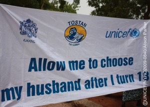 A banner bearing the slogan Allow me to choose my husband after I turn 18, and the logos of the Government, the NGO Tostan and UNICEF, advocates against early marriage. It is being displayed at an event in Darsilameh Village renouncing FGM/C and early marriage in 24 communities in eastern Upper River Region. The change in community practice of these traditional norms came about through their participation in the Community Development and Empowerment Programme, supported by the Government, the NGO Tostan and UNICEF. On 14 June 2009 in the Gambia, women representing 24 neighbouring villages in Upper River Region gathered in Darsilameh Village to announce and celebrate an end to the practices of female genital mutilation/cutting (FGM/C) and early marriage in their communities. An estimated 3 million African girls in 28 countries are subjected to FGM/C every year, a social convention linked to traditional perceptions of girls status for marriage. But FGM/C also causes great suffering and often life-long and life-threatening health risks. FGM/C and other pervasive practices such as early marriage are now recognized as manifestations of gender inequalities that threaten the well-being of girls and women and increase maternal health and child mortality risks. In the Gambia, 78 per cent of girls/women aged 15-49 years have been subjected to FGM/C; a figure that rises to 99 per cent in the Upper River Region. Likewise, almost half of Gambian girls marry before age 18. The 14 June celebration is part of a process, now underway in several African countries, of changing harmful and gender-discriminating social norms through a human rights-based approach, in which knowledge and support are offered to encourage positive change that is directed by community members themselves. In Upper River Region, some 80 communities mainly from the Mandinka ethnic group are participating in this process through the Community Development and Empowerment Programme, implemented by the Government, the international NGO Tostan and UNICEF. Public declarations renouncing harmful practices are a critical part of the process, affirming a communitys commitment and helping to create a critical mass for nationwide change. More than 600 people including girls and women, religious leaders, village chiefs, delegates from youth and womens groups, government officials and representatives from Tostan and UNICEF attended the Darsilameh celebration.