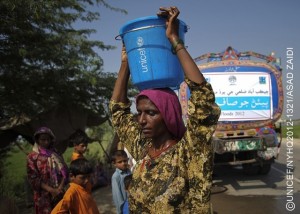 A woman carries a bucket filled with safe water that she was given during a water distribution from a tanker-truck, on the Jamali Bypass, the main highway in Jacobabad District, in Sindh Province. The truck bears the logos of UNICEF and other support partners. More than 58,600 flood-affected people in the province have received safe drinking water via tanker trucks. By mid-October 2012 in Pakistan, monsoon rains and torrential flooding that began in early September had affected more than 5 million people  primarily in the provinces of Sindh, Punjab and Balochistan. Over 459,000 homes as well as roads and schools have been damaged or destroyed; some 265,000 people remain displaced in relief camps, with many others living in roadside and other informal settlements; over 1.1 million acres of land and an estimated 54 per cent of health facilities have been affected; and numerous water sources have been contaminated. More than 80 per cent of the affected are women and children under age 14 in need of shelter, food, safe drinking water, sanitation, maternal and child health care and malaria prevention. Malnutrition rates in the hardest hit districts are well above the emergency threshold, and 74 per cent of children in affected communities are out of school. Logistical constraints are hampering relief efforts in many areas, and continuing insecurity is placing United Nations staff and other humanitarian workers at increased risk. In response to the crisis, UNICEF is working with the Government (which has pledged US $91 million to the monsoon floods response), as well as with other UN agencies and partner NGOs. Support includes the provision of: essential child and maternal health services; therapeutic and supplementary feeding programmes; safe drinking water, sanitation facilities and hygiene kits; ongoing immunization services, including to eradicate polio; temporary learning centres and child-friendly spaces; and protective services for children, including for family reunification and psychosocial support. UNICEF is requesting US $15.4 million to fund its part of the response over the next three months.
