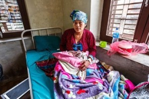 Patali sits on a cot while holding her 3-hour-old son sit in the UNICEF-supported Trishuli Hospital, in the city of Bidur, Nuwakot District. The hospital was heavily damaged during the massive earthquake and is now running its delivery room  where Patali was able to give birth  in a different wing of the facility that did not sustain damage. UNICEF has provided hospital tents, tarpaulins, delivery kits, hygiene kits and medicines for the medical facility. Patalis home was destroyed in the quake; her husband plans to find rental accommodations for the family. On 9 May 2015 in Nepal, recovery efforts continue following the massive 7.8-magnitude quake that struck on 25 April, leaving over 7,000 people dead and destroying nearly 191,000 houses. Residences, schools and vital infrastructure, including hospitals, have been severely damaged or destroyed, leaving children and families homeless, vulnerable to disease outbreaks and in urgent need of food, shelter, safe water and sanitation, and health support. Access to quality maternal and newborn health care in Nepal was limited even before the earthquake, but the natural disaster exacerbated the situation  many birthing centres across the most affected districts of Nepal have been damaged or destroyed, leaving many pregnant women without access to the care they need to ensure the safe delivery of their babies. UNICEF and partners are working around the clock to deliver aid to children and women, including by setting up emergency birthing centres across affected areas.