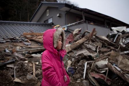 A young child looks at her house destroyed in the tsunami devastated town of Rikuzen-Takaata, Iwate Prefecture, Japan March 15, 2011. Thousands of people died in this small town 70 km north east of Sendai where they ran out of body bags.