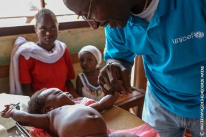 UNICEF Representative in the Central African Republic Souleymane Diabaté plays with a baby at the ADECOM (Association for Community Development) health post in the Bogbaya neighbourhood in Bangui, the capital, during the measles vaccination campaign. A woman and another child are seated nearby. Children are also receiving vitamin A and deworming tablets during the campaign. Mr. Diabatés shirt bears the UNICEF logo. From 22 to 26 May 2013 in the Central African Republic, an emergency measles vaccination campaign is being held after eight children in Bangui, the capital, tested positive for the disease in April. The campaign is being implemented by the Ministry of Health, the World Health Organization (WHO), UNICEF and other partners and aims to immunize an estimated 125,000 children under age 5. Measles remains a leading cause of death among young children worldwide. In the Central African Republic, one of the worlds poorest countries, the measles vaccination rate stands at a low 62 per cent. Recent conflict has also contributed to a further eakdown in health and other services and put hundreds of thousands of children at risk of the disease. An estimated 246,500 vaccines have been despatched to Bangui in response to the outeak, and to improve routine measles vaccination in the countrys high-risk regions. In response to the current crisis, UNICEF is supporting emergency health activities in Banguis four main hospitals and at health centres throughout the country (including health supplies for up to 141,000 people for three months), as well as interventions in the areas of nutrition, water, sanitation and hygiene (WASH), education and child protection.