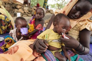 (Foreground) Mariam, 15, feeds her 10-month-old sister, Fatouma, from a package of Plumpynut, at the UNICEF-supported outpatient feeding centre in the town of Bitkine, Guera region. Plumpynut, a brand of ready-to-use therapeutic food, is a high-protein, high-energy, peanut-based, packaged paste for malnourished children that does not require cooking or handling. Behind them, Aljema, 8, feeds another type of therapeutic food to Toma, her younger sister.