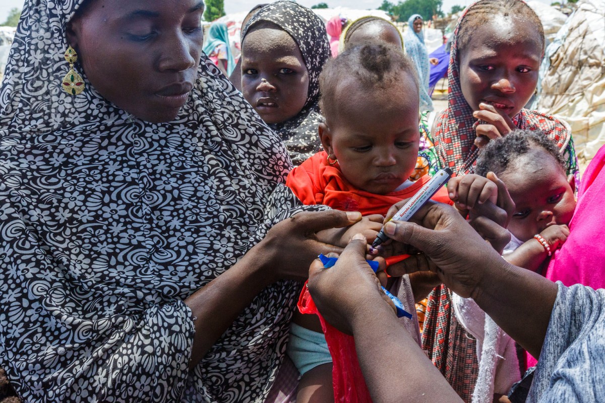 On 15 August 2016 in Muna Garage IDP Camp, Borno state, Nigeria, a UNICEF health worker uses a pen to mark the thumb of Ajeda Mallam, 6 months, who has just been vaccinated against polio at a camp for internally displaced persons outside Maiduguri northeast Nigeria. It is her first vaccination, having been born under Boko Haram captivity. UNICEF and partners have started an emergency polio immunization campaign in Borno State, as a result of two wild poliovirus cases recently found among children in the conflict-affected area. Nigeria  and the continent  had its last confirmed polio case two years ago and was within a year of being certified polio-free.