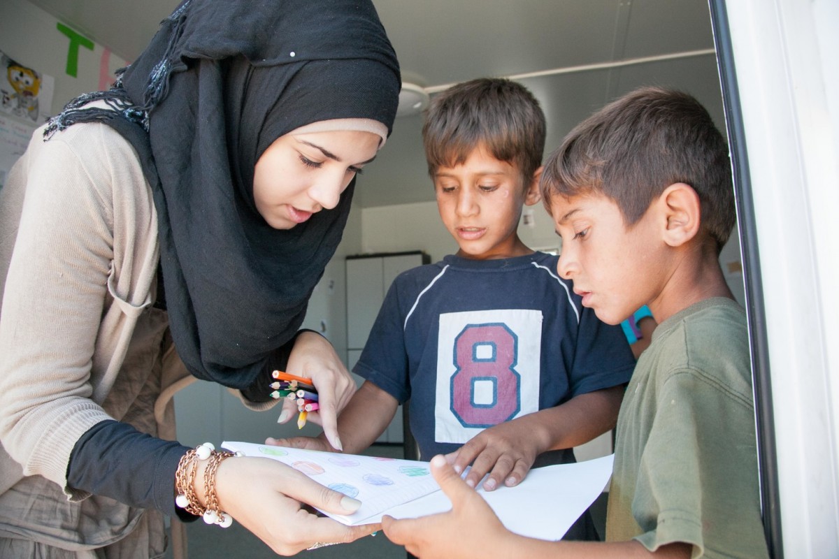 On 18 August 2016 in Athens, Greece, children attend school for 40 minutes each day in the Skaramagas refugee camp.  Isra Alsabsabi (left), 19, a refugee from Aleppo, Syria teaches in English and Arabic.  Her younger sisters (not pictured), Sarah, 12, Salaam, 8, Sham, 8, also attend the school where Esraa teaches.  Isra's family escaped Aleppo in 2013 and spent nearly three years in Altinozu, Antakya, in Turkey not far from the Syrian border.  Her father is already in Germany and the rest of the family are still stranded in Greece. 

Several refugee teachers are teaching some 650 refugee children at the UNICEF-supported Greek NGO, Pireaus Open School, that is providing classroom supplies, teachers and technical assistance for formal education in the camp.  From 9:00am until 6:00pm classes lasting 40 minutes each are intended to reach the greatest number of children.  Next month, UNICEF will bring in 11 more classroom containers with additional supplies.   

With the sudden increase of arrivals, hundreds more refugee and migrant children are becoming stranded in Greece with critical needs such as education and protection, says UNICEF. More people arrived in the first three weeks of August than all of July 2016 (1,920 for July; 2,289 as of 24 August). This new influx comes at a time when Greece is struggling to cope with a strained welfare system due to the ongoing economic crisis, leaving refugee and migrant children facing a double crisis. In total, children make up nearly 40 per cent of the current stranded population.

Getting children into education is a key priority for UNICEF and its partners in Greece, especially in the light of recent reports of children at risk. UNICEF has been supporting learning and recreational activities for refugee children in Skaramangas camp, near Athens, with the Greek NGO Piraeus Open School for Immigrants, as well as providing 11 container classrooms. UNICEF education programmes are being scaled up beyond Attica to other camps, tar