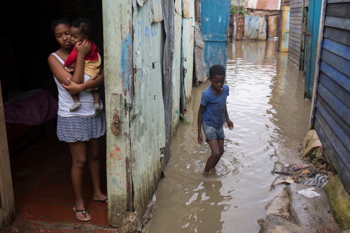 On 4 October 2016, at their doorstep, a mother with her two children look at the flooded neighbourhood of los Guandules, in Santo Domingo. Hurricane Matthew passed over Dominican Republic today with heavy rains, killing four people, including three children. It is estimated that many children and families have been displaced from their homes, in Haiti, Jamaica and Cuba, including 18,000 people in the Dominican Republic.