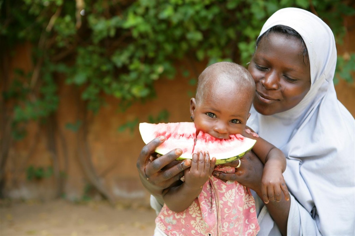 28 September 2010, a mother holds her child while eating a slice of watermelon in Niamey the capital of Niger. In Niger many common childhood killer diseases such as diarrhoea, acute respiratory infections and malaria can be prevented with increased knowledge and adoption of key family practices such as exclusive breastfeeding up to six months, birth spacing, proper use of oral rehydration therapy and complementary food and regular hand washing among others. UNICEF and its partners work at the institutional, community, household and health facilities levels to promote the adoption of key family practices through community-driven initiatives and via the combination of traditional and modern communication channels to raise awareness on the links between poor hygiene, water and sanitation and the spread  of diseases in populations.