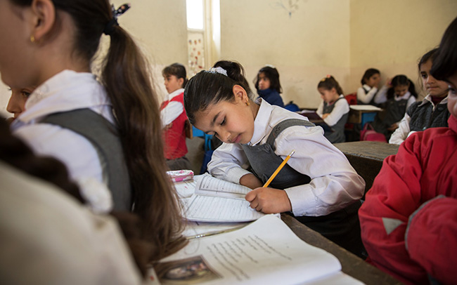 Isra take notes in class. Her family was displaced from twice before arriving in Erbil, Iraq, causing her to miss a year of schooling.