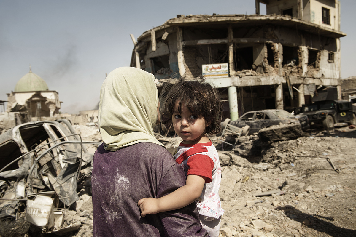 A woman carries her child through the debris of buildings and vehicles destroyed during intense fighting as they flee the Old City for safe areas in Mosul, Iraq, Thursday 6 July 2017. Partially visible at left is the destroyed Great Mosque of al-Nuri.

The end of the violence in Mosul in July 2017 is likely to be a turning point for Iraq, but it will not bring the guns to silence as the battle will soon turn to Tal Afar, West Anbar and Hawija. Three years of traumatic experiences and months of intense fighting have left children and families in Mosul struggling with the physical and psychological wounds of war, with childhoods turned into nightmares of brutality, displacement and loss. Many are being treated in trauma centres in west Mosul with bullet and shrapnel wounds are children and many children who fled the intense fighting between government and non-government actors are severely distressed and need psychosocial care. Warring parties actively recruited children into the fighting, depriving them of a normal childhood and the chance of a better future.Some children are being held in detention centres. UNICEF is providing these children with legal representation, education, psychosocial assistance, vocational training, and helping to improve the conditions of the facilities where children are held. Providing schools, water, sanitation and health services will be crucial for all Iraqi children and their families to return home. Otherwise, the risk is not only of a lost generation, but also severely restricted opportunities to build a solid foundation for coexistence, tolerance and peace in the future.