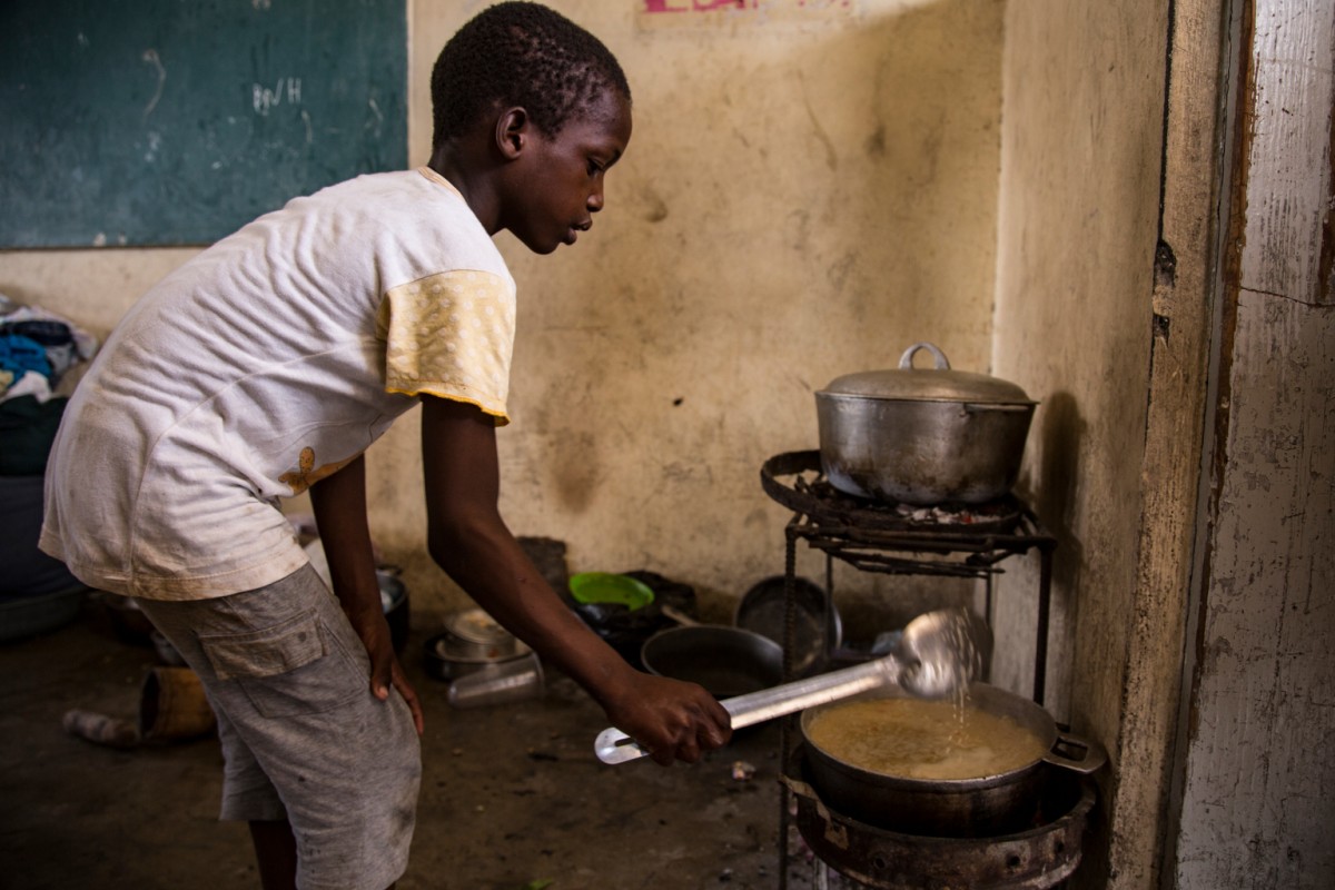On 14 October 2016, a boy cooks at a school in Les Cayes, Department du Sud, Haiti.  Ecole Pierre Guerrieris currently in use as a living space or shelter for several hundred people who have lost their homes to hurricane Matthew. Although the school year should have begun, all public schools in the area hit by the hurricane remain closed or turned over to the displaced. Hurricane Matthew passed over Haiti on Tuesday October 4, 2016, with heavy rains and winds. While the capital Port au Prince was mostly spared from the full strength of the class 4 hurricane, the western area of Grand Anse, however was in the direct path. The cities of Les Cayes and Jeremie received the full force sustaining wind and water damage across wide areas. Coastal towns were severely damaged as were many homes in remote mountainous regions. International relief efforts are underway to provide food water and shelter to the people affected by the storm.An estimated 500,000 children live in the Grande Anse Department and Grand South Department in southern Haiti, the areas worst hit by Hurricane Matthew. UNICEF had prepositioned emergency supplies with national authorities to reach up to 10,000 people. On 8 October, six water trucks arrived in Jeremie and Les Cayes, the respective capital cities within the Departments. Additional water and sanitation supplies, such as water purification tablets, water bladders and plastic sheeting, have been dispatched to the most affected departments in the westernmost tip of Haiti. As of 10 October, UNICEF delivered blankets, buckets, water purifying equipment and cholera diagnostic kits. UNICEF is working to reinforce good hygiene practices, especially in temporary shelters, in order to minimize the outbreak of disease. An investigation is underway to confirm the areas affected by cholera, and to determine the cross-over with hurricane-affected areas.
